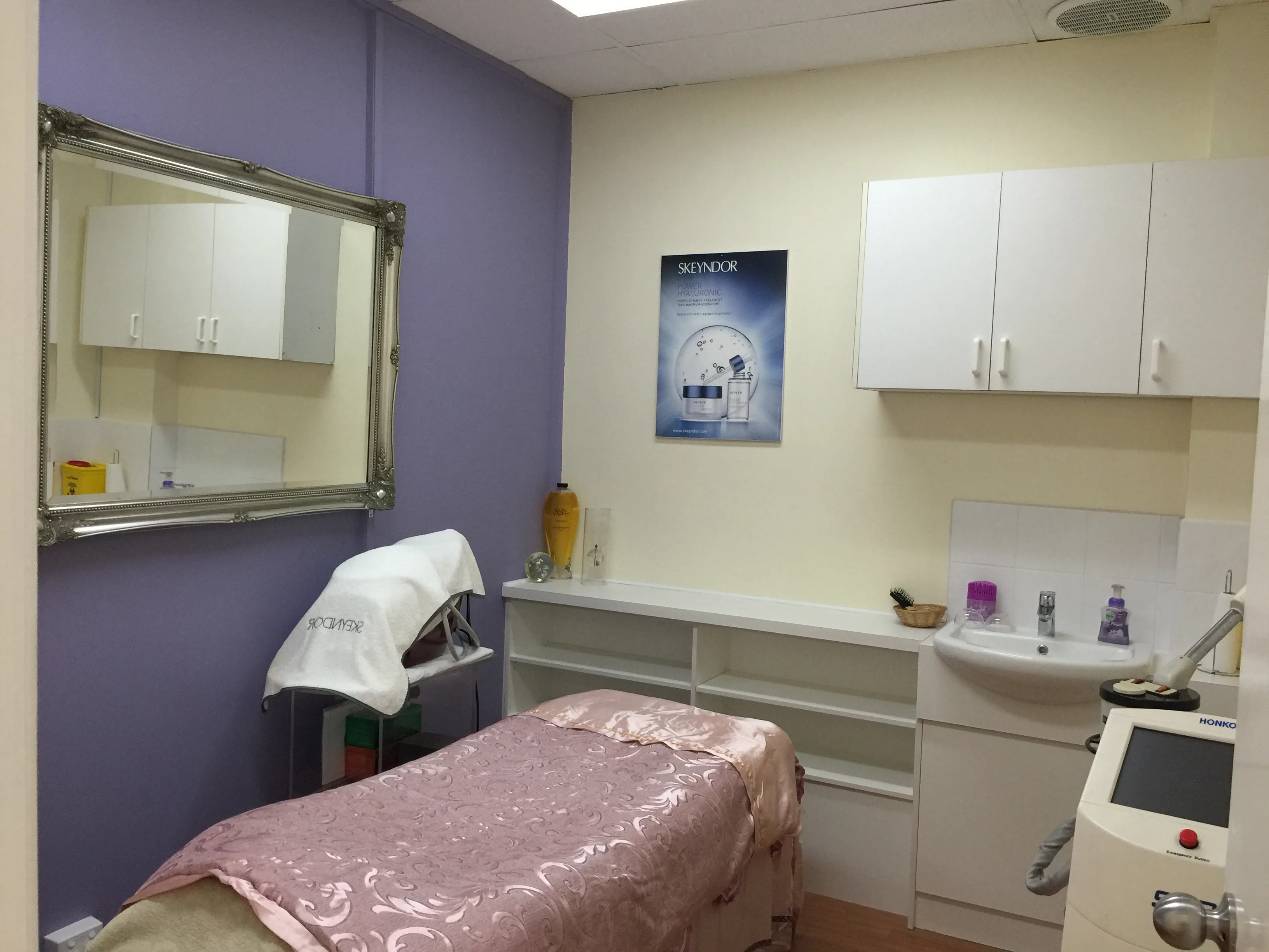 Private treatment room — lilac walls, ornate mirror, satin-draped treatment bed, Skeyndor poster and laser device