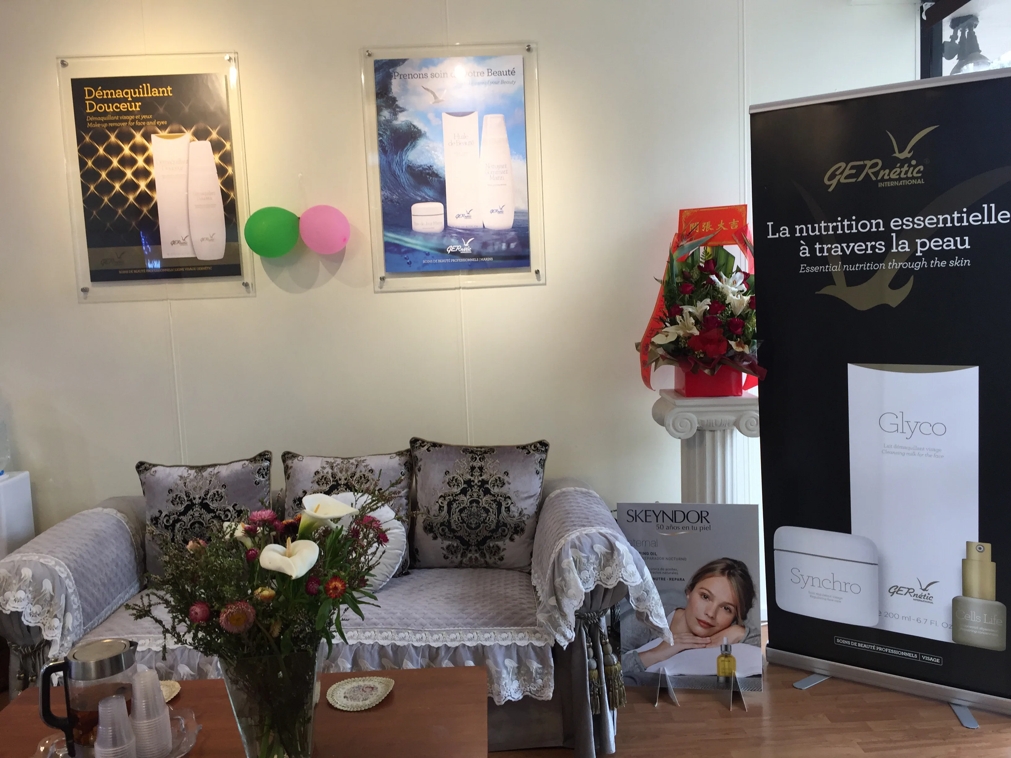 Waiting lounge — grey damask sofa with lace throws, fresh flowers, Gernetic and Skeyndor product banners