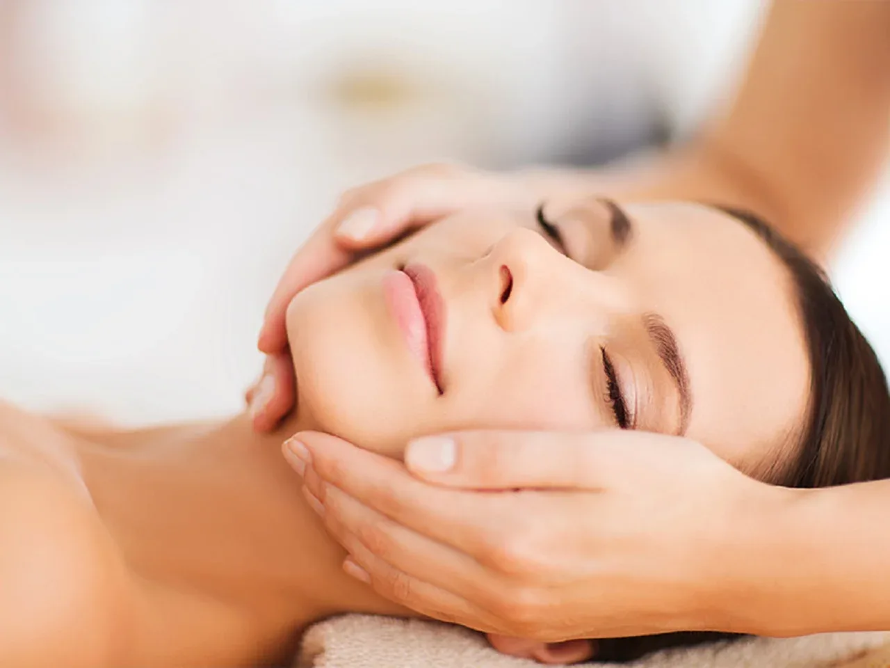 Professional facial treatment, therapist hands working on client's face in a bright room