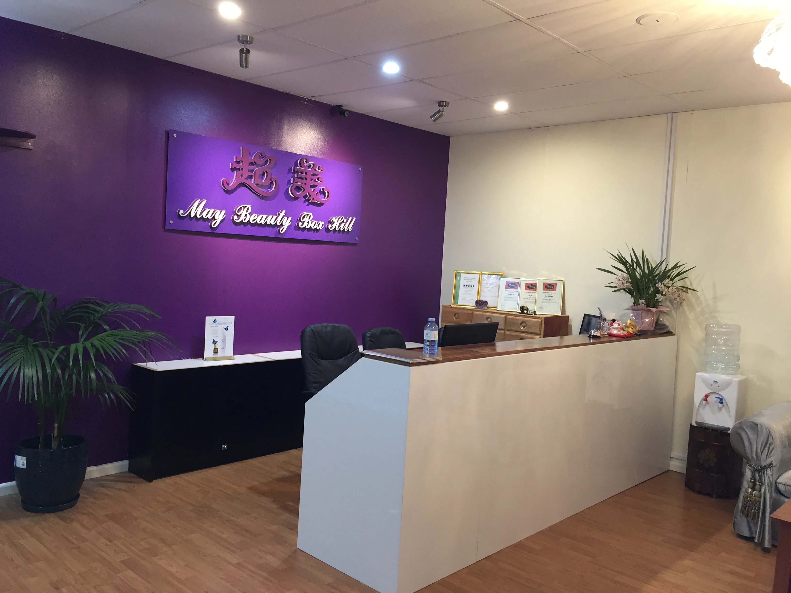 May Beauty Box Hill reception — deep-purple feature wall with illuminated pink-script sign, welcome desk, orchid, timber floor