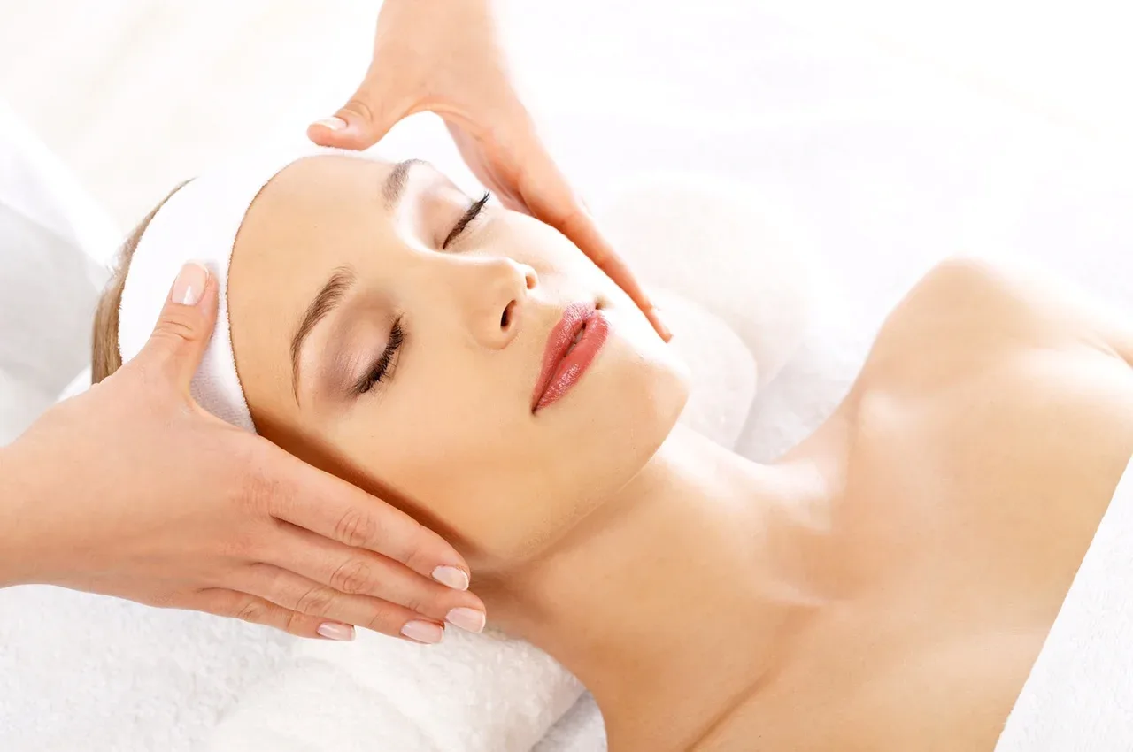 Skin care treatment — therapist hands on forehead in a high-key white treatment setting