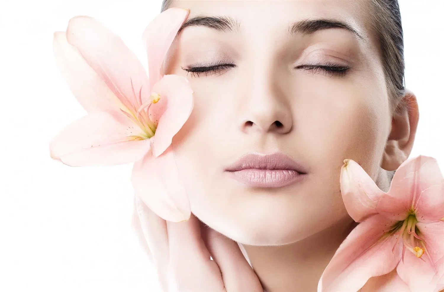 Relaxed woman with pink lilies against her cheek, eyes closed, clean skin