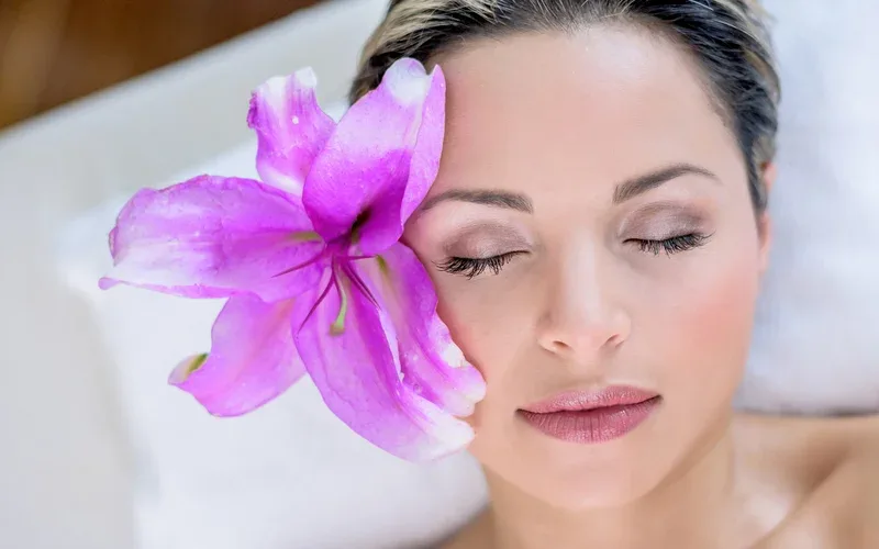 Woman resting with a purple lily and spa towel — a moment of calm beauty care